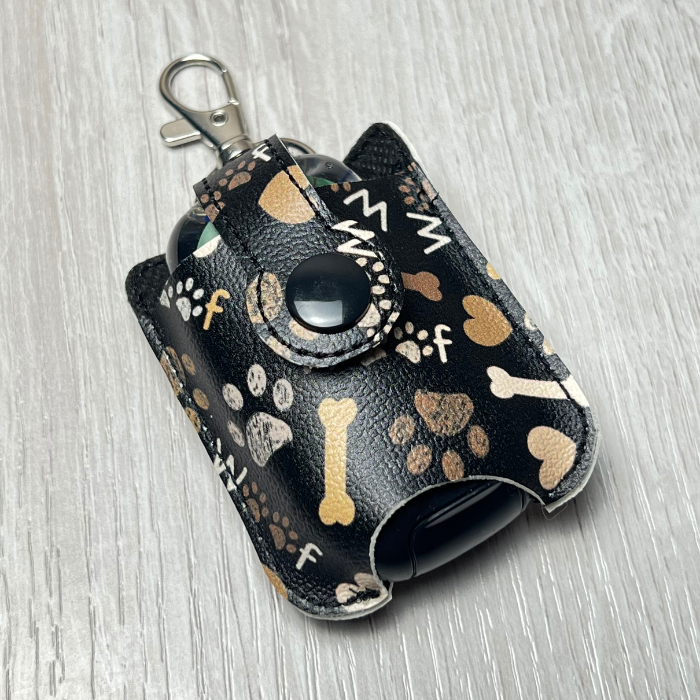 Hand sanitizer holder keychain in black patterned vinyl with "woof," paw prints and dog bones