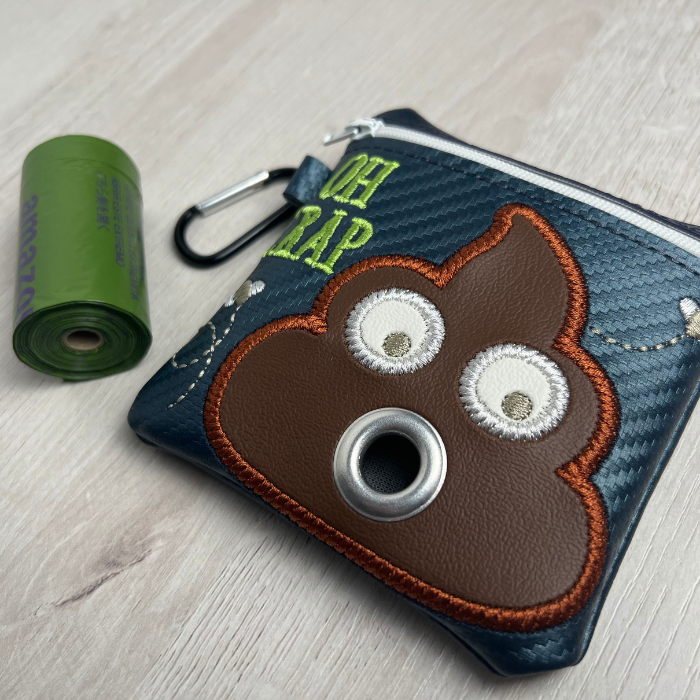 Blue poop bag holder with saying "oh crap." Embroidered brown surprised poop face and two flies flying around it.